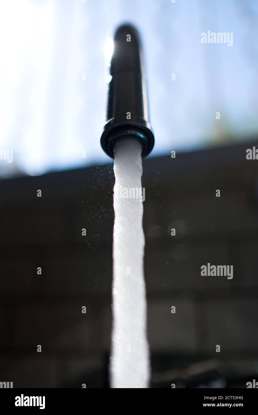 closeup of water pouring out of a kitchen tap with a open window in the background Stock Photo