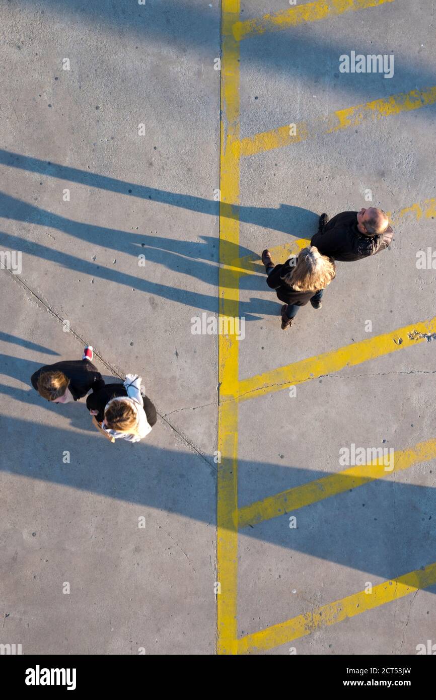 aerial view of two adult couples respecting social distancing by walking either sides of a pavement, painted with yellow warning lines, Southern Franc Stock Photo