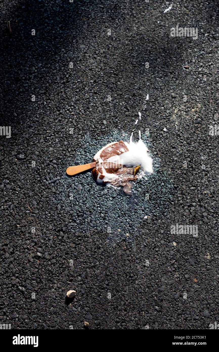 looking down at a fallen squashed and melting chocolate vanilla ice cream lolly on a freshly tarmacked road in a french city. Montpellier, France Stock Photo
