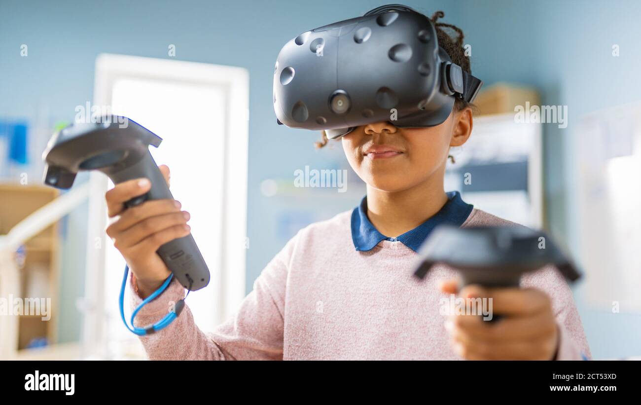 Elementary School Computer Science Class: Cute Girl Wearing Augmented Reality Headset and Using Controllers Learns Lessons in Virtual Reality Excited Stock Photo