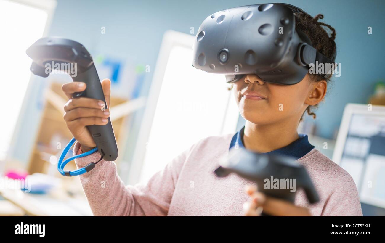 Elementary School Computer Science Class: Cute Girl Wearing Augmented Reality Headset and Using Controllers Learns Lessons in Virtual Reality Excited Stock Photo