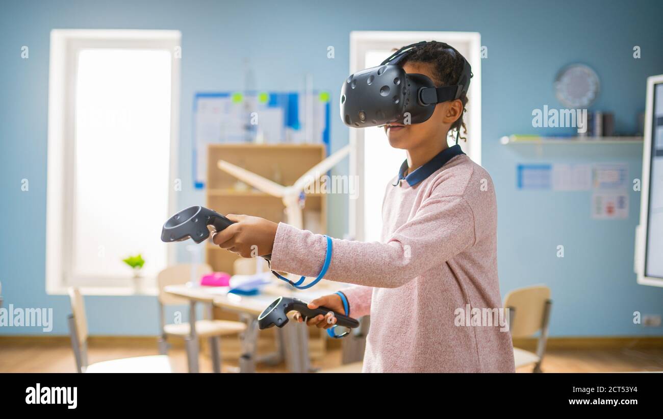 Elementary School Computer Science Class: Cute Girl Wearing Augmented Reality Headset and Using Controllers Learns Lessons in Virtual Reality Excited Stock Photo