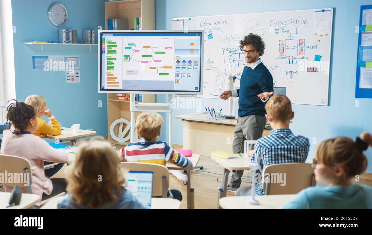 Elementary School Science Teacher Uses Interactive Digital Whiteboard to Show Classroom Full of Children how Software Programming works for Robotics Stock Photo