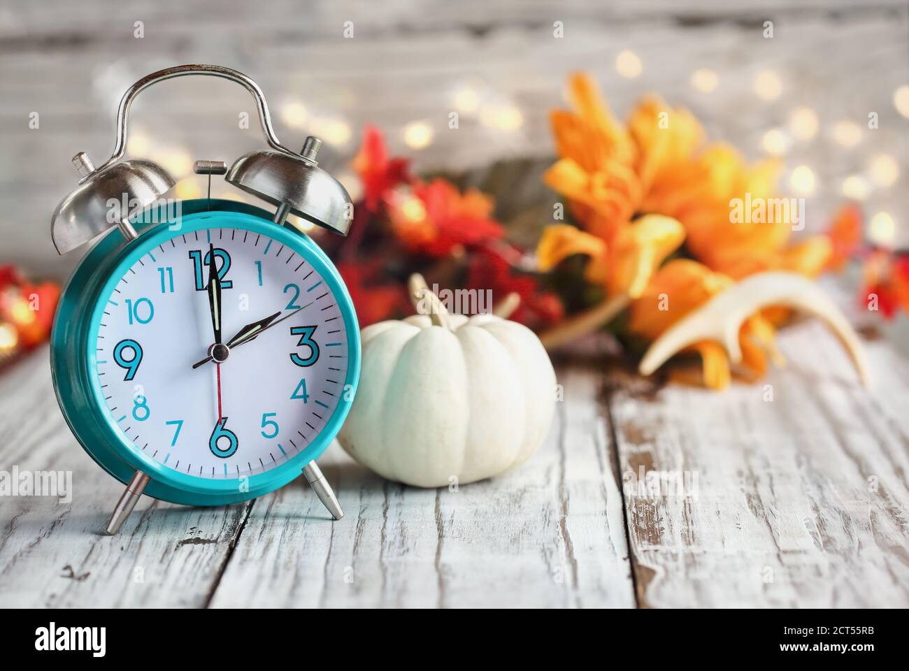 Set your clocks and fall back. Clock and decorations of mini pumpkins, colorful autumn leaves, antlers and bokeh lights over a white wooden table. Day Stock Photo