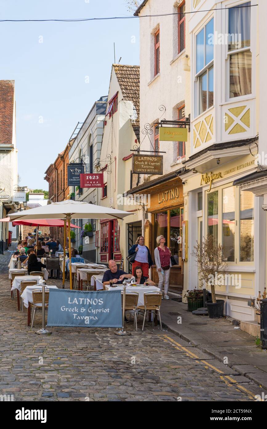 People enjoy an al fresco meal on a warm sunny day, seated at pavement tables outside the restaurants in Church Lane, Windsor, Berkshire, England, UK Stock Photo