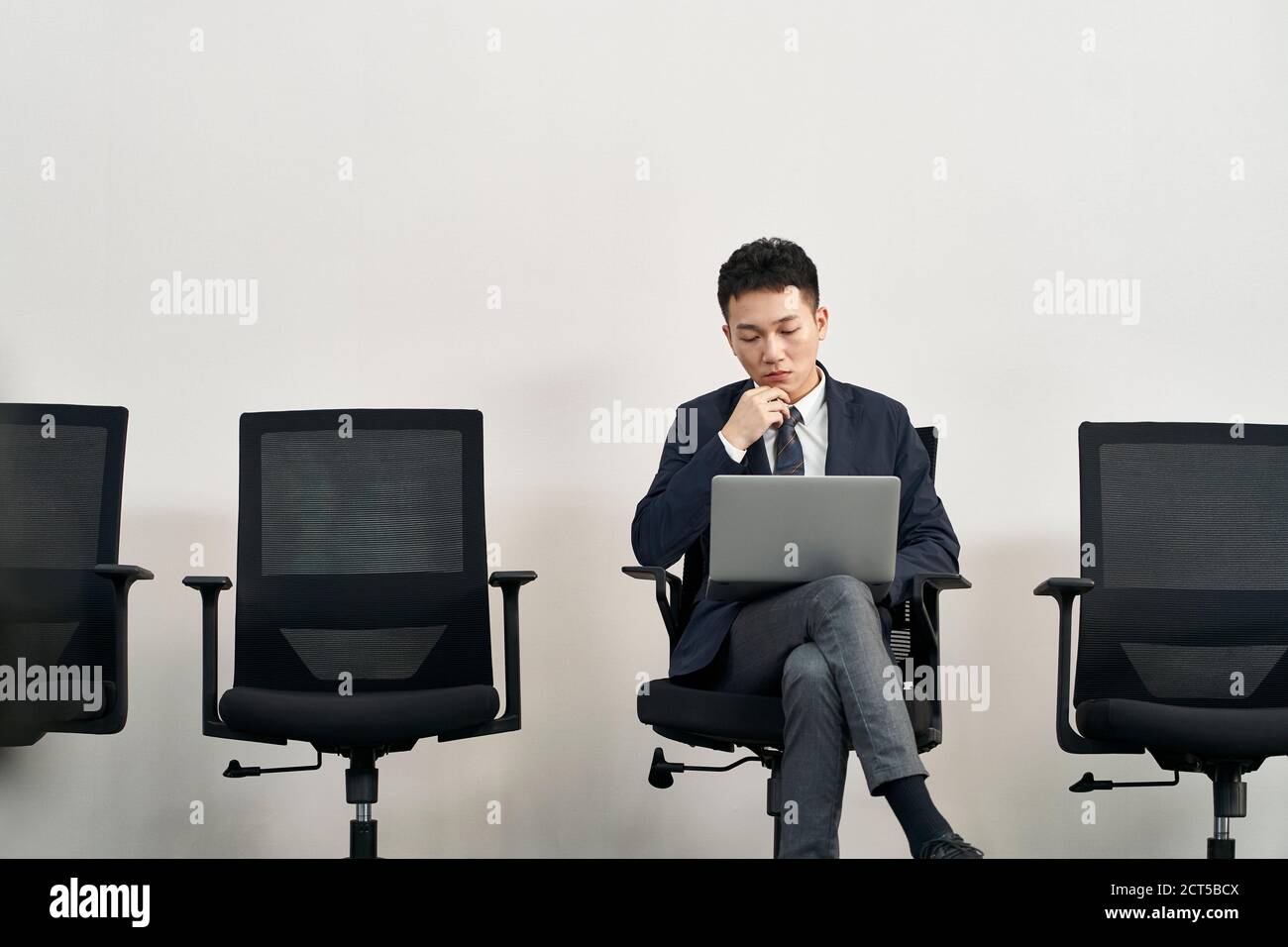young asian job seeker sitting in chair preparing for interview using laptop computer while waiting in line Stock Photo