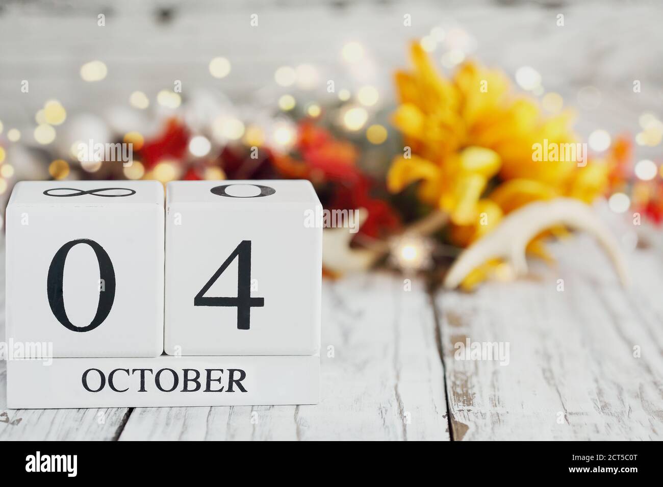 White wood calendar blocks with the date October 4th and autumn decorations over a wooden table. Selective focus with blurred background. Stock Photo