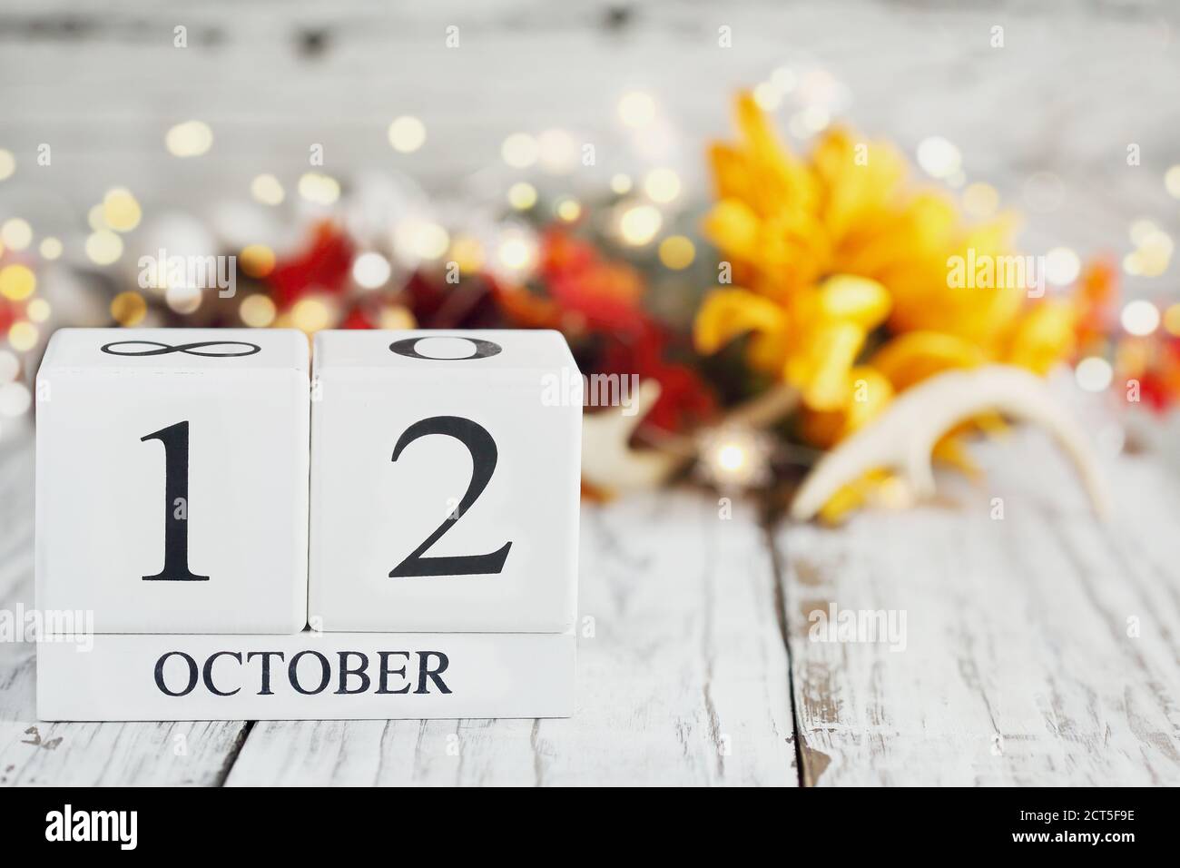White wood calendar blocks with the date October 12th and autumn decorations over a wooden table. Selective focus with blurred background. National Fa Stock Photo