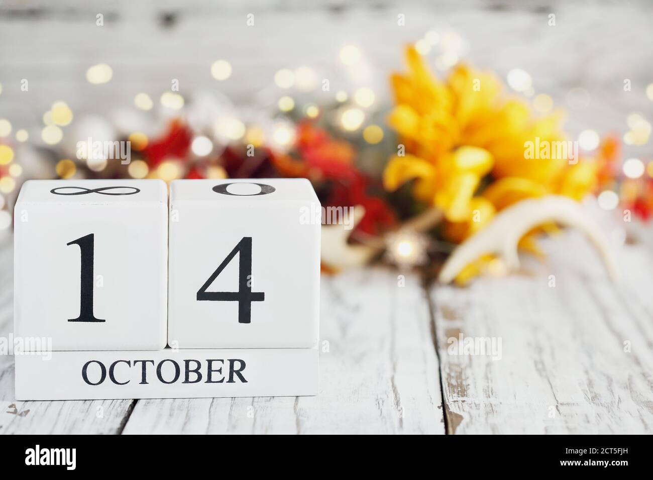 White wood calendar blocks with the date October 14th and autumn decorations over a wooden table. Selective focus with blurred background. Stock Photo