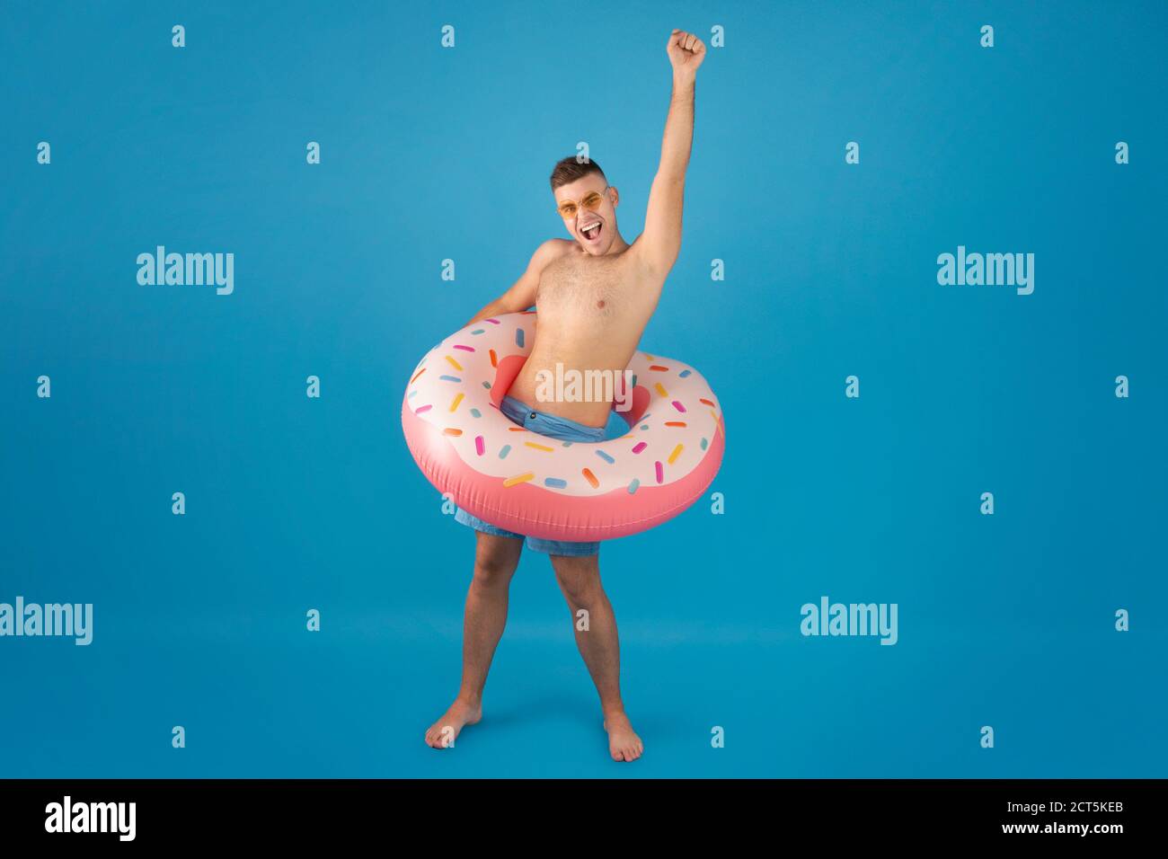 Full length portrait of handsome millennial man wearing inflatable ring and making YES gesture over blue background Stock Photo