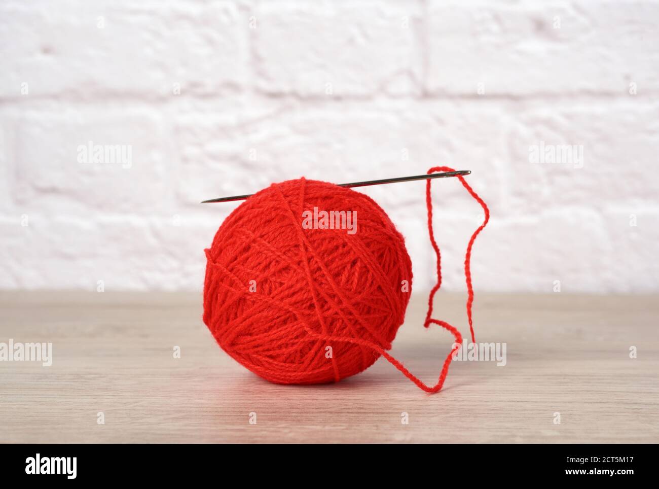 red ball with woolen thread and large needle on white brick wall ...