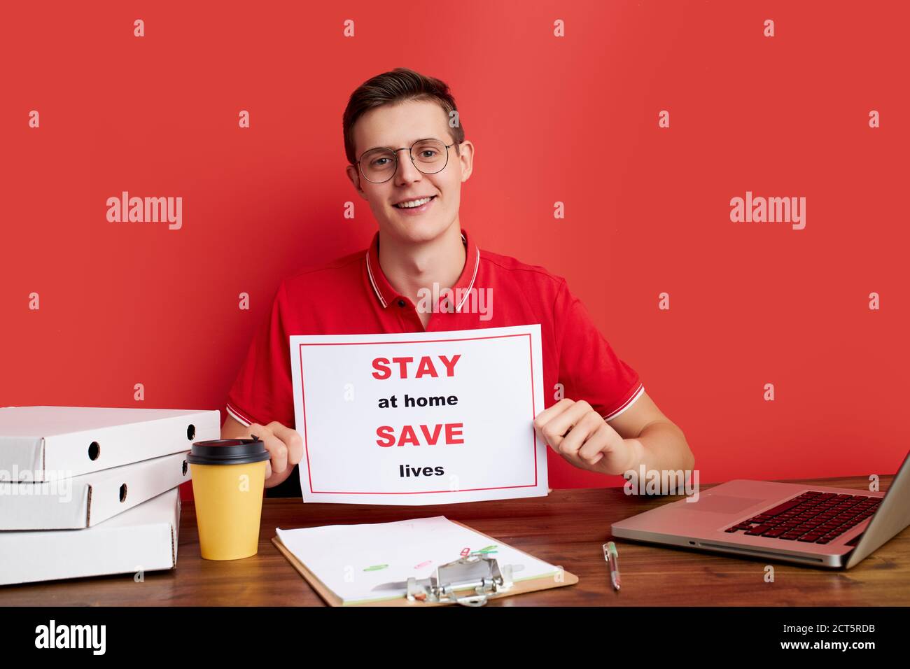 open-minded caucasian male ask people stay home during quarantine, work with laptop, at freelance, isolated red background Stock Photo