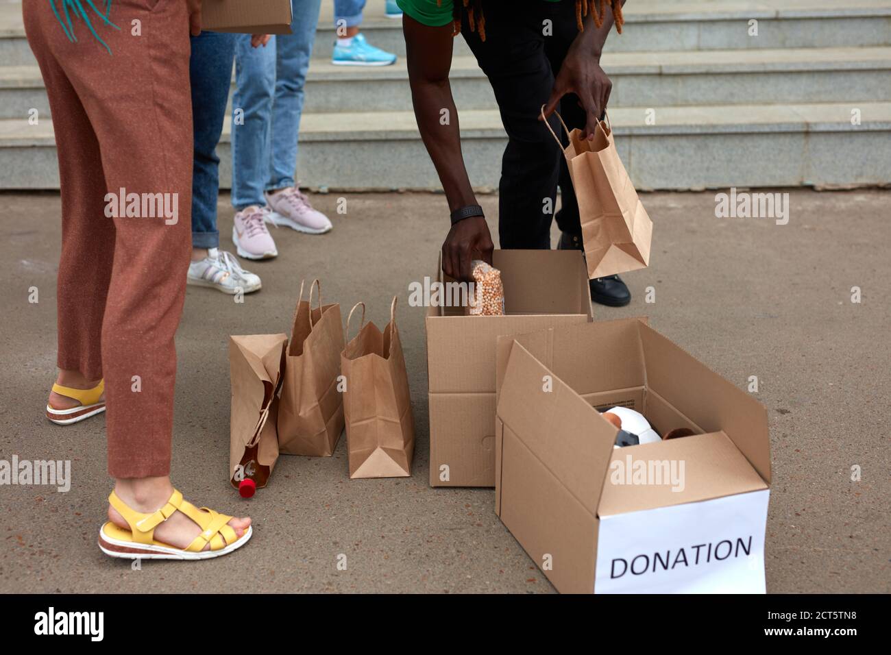 group of diverse people sort through donated food items while volunteering in community, they use cardboard boxes for collecting donation Stock Photo
