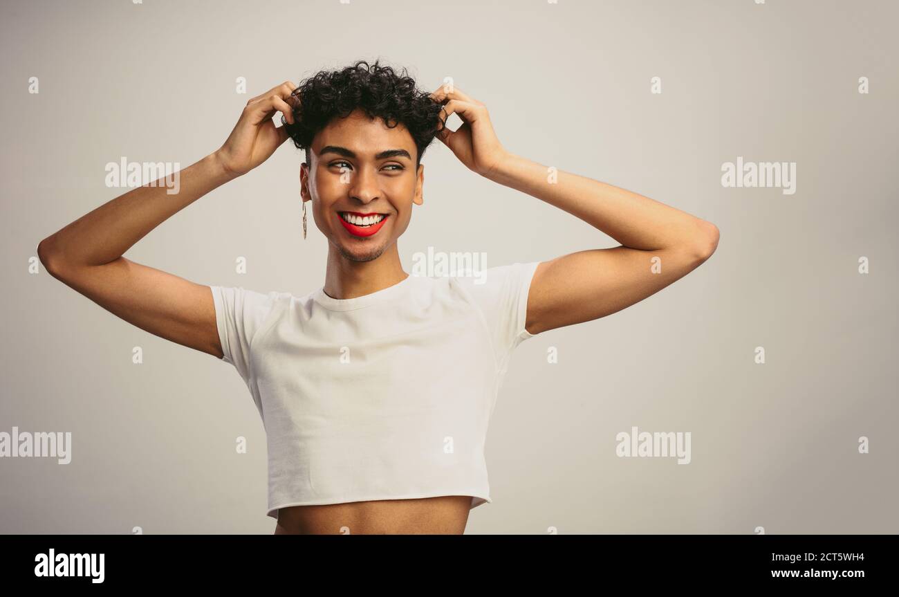 Gender fluid man wearing crop top with his hands in hair against white background. Gay man looking away and smiling. Stock Photo
