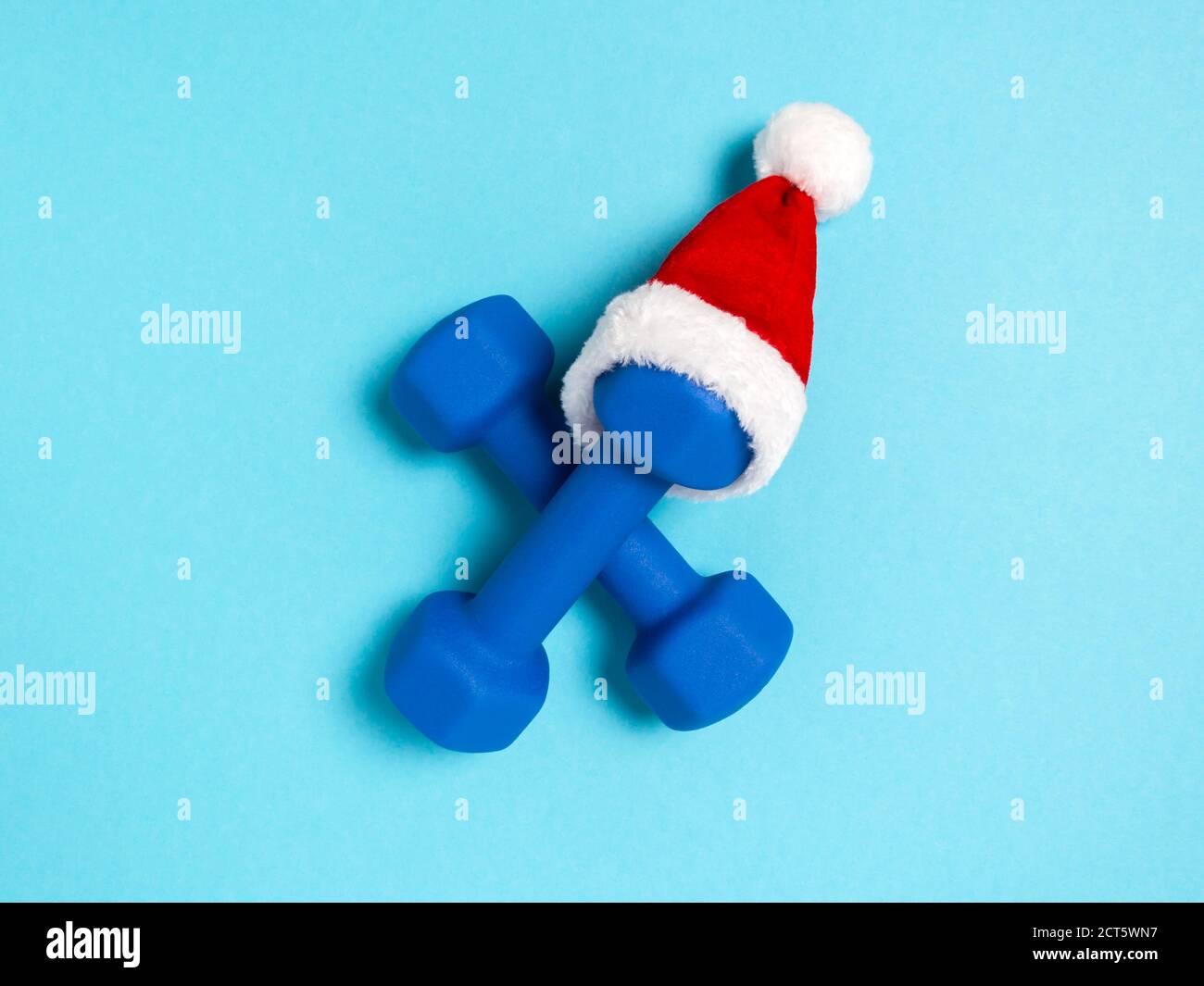 Christmas sports flat lay with dumbbells in red Santa's hat on blue background. Christmas and new year holiday concept for fitness, workout and health Stock Photo
