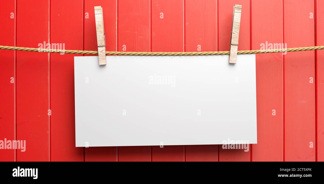 Empty paper card holding on rope with two clothespins on red wooden background. Blank memo, reminder, sign template. 3d illustration Stock Photo