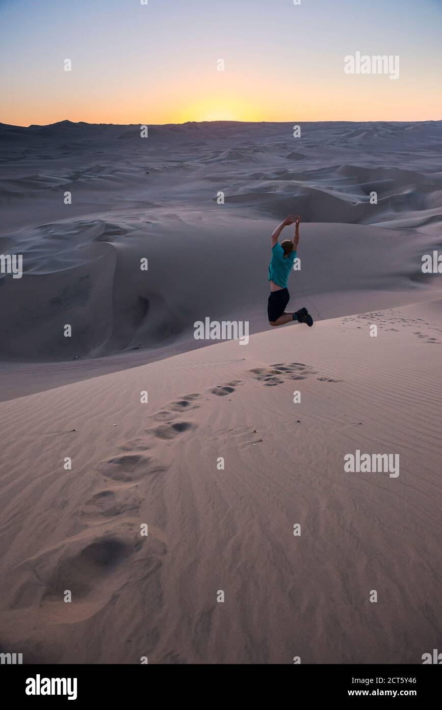 Peru Jumping Rocks Tourist jumping in the desert at sunset at Huacachina, Ica Region, Peru ...