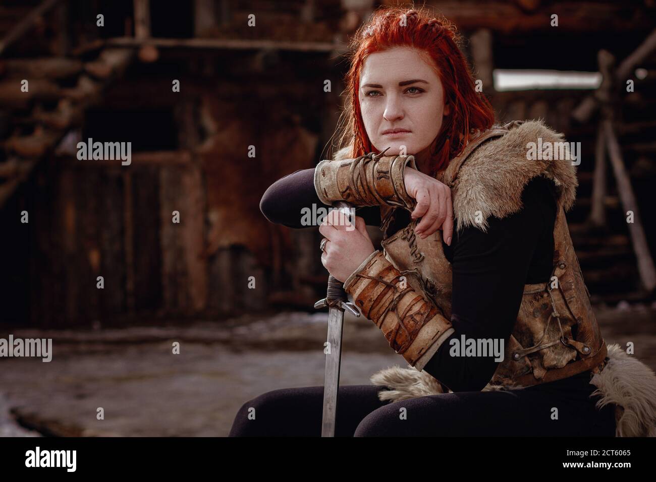 Viking woman with red hair. In the hands of the sword to fight the enemy.  Reconstruction of a medieval scene. Against the backdrop of a large viking  Stock Photo - Alamy