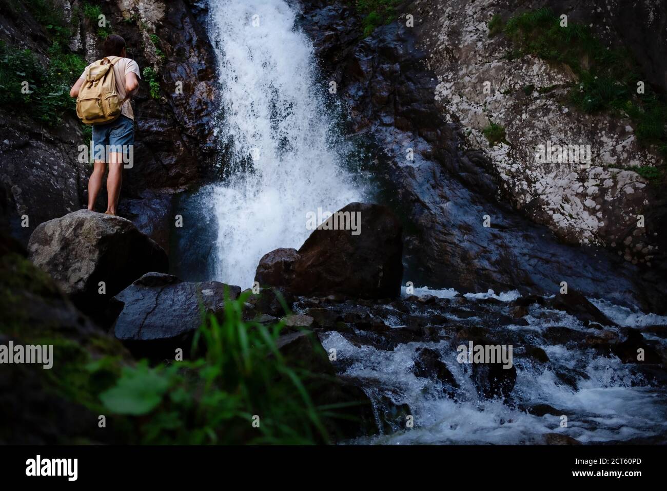 Hiker waalkinh with backpack looking at waterfall in park in beautiful nature landscape. Portrait of male adult back standing outdoor. Waterfall Shumk Stock Photo