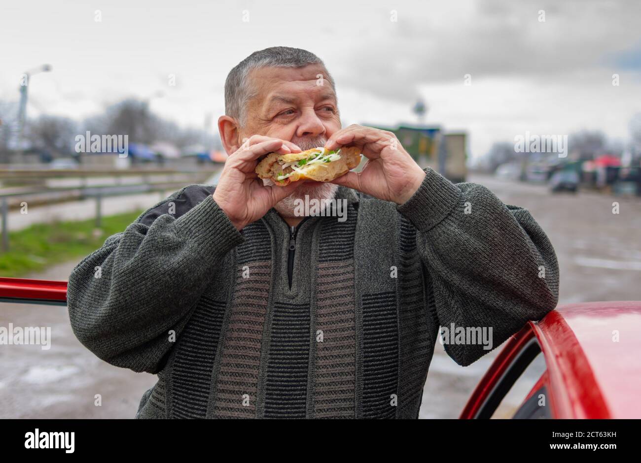 Caucasian senior driver gobbling lyulya kebab in lavash leaning his elbow on the car roof Stock Photo