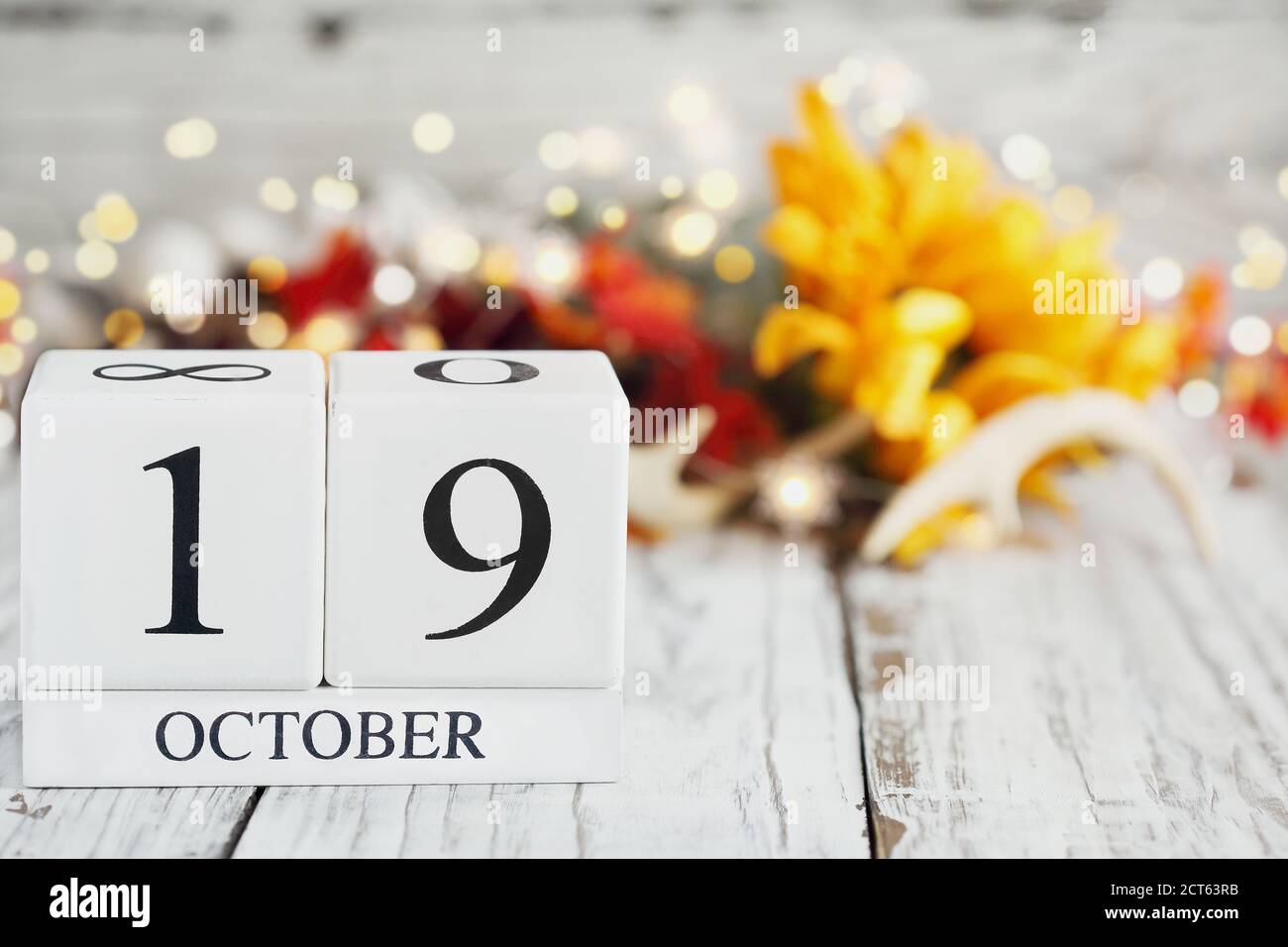 White wood calendar blocks with the date October 19th and autumn decorations over a wooden table. Selective focus with blurred background. Stock Photo