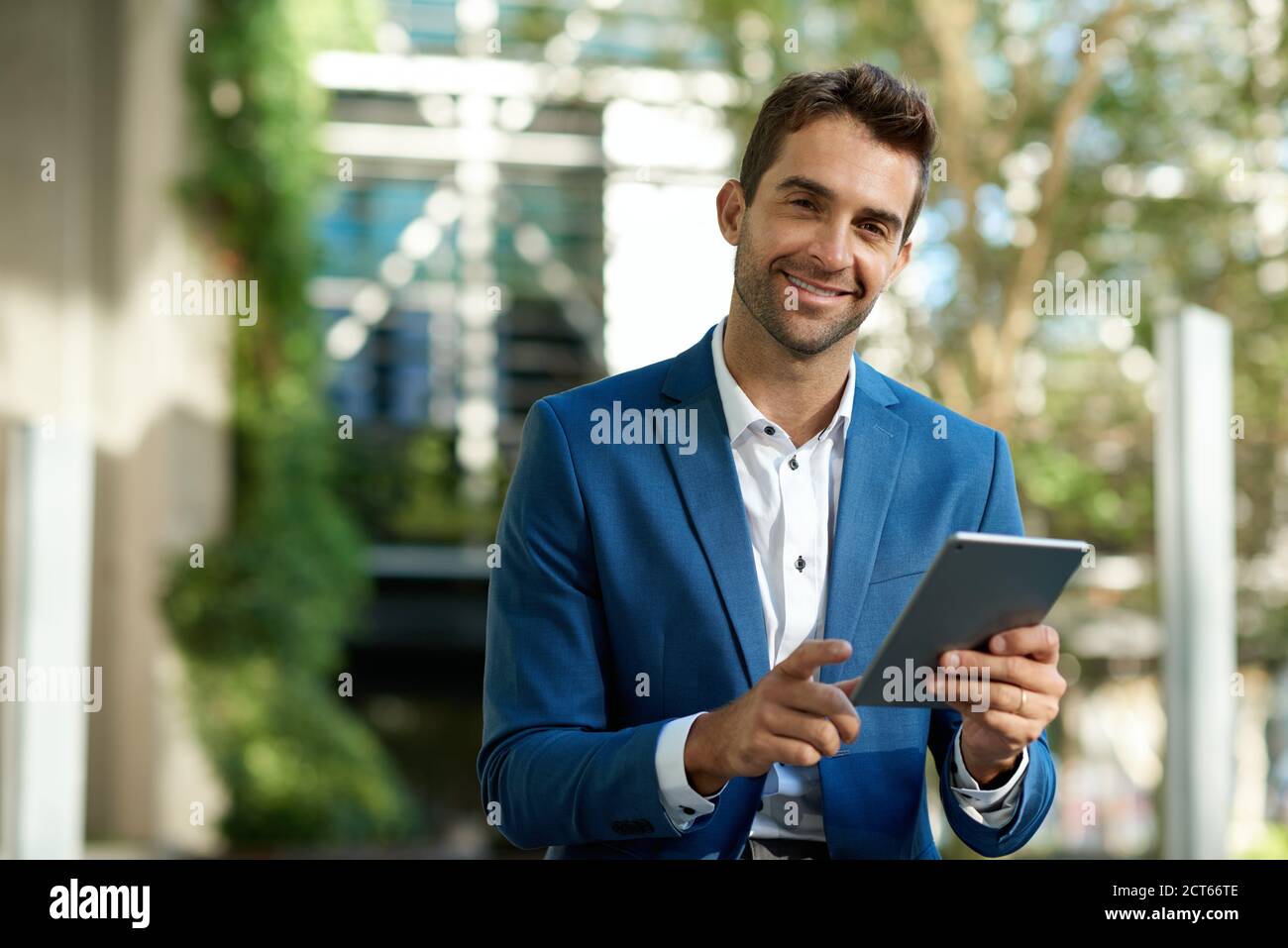 Smiling young businessman using a digital tablet while standing outside Stock Photo