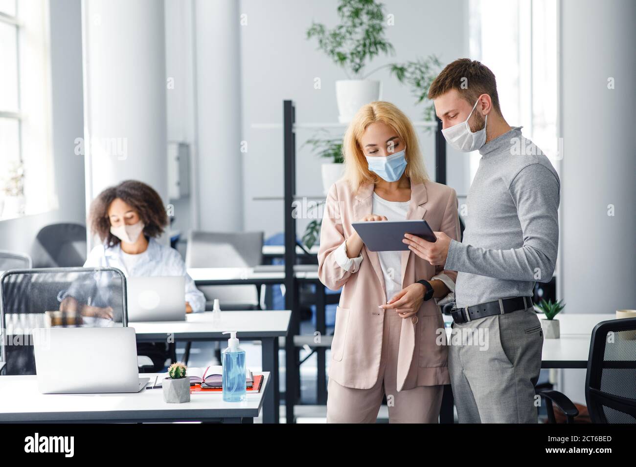 Colleagues in protective masks discuss project and look at tablet in coworking office Stock Photo