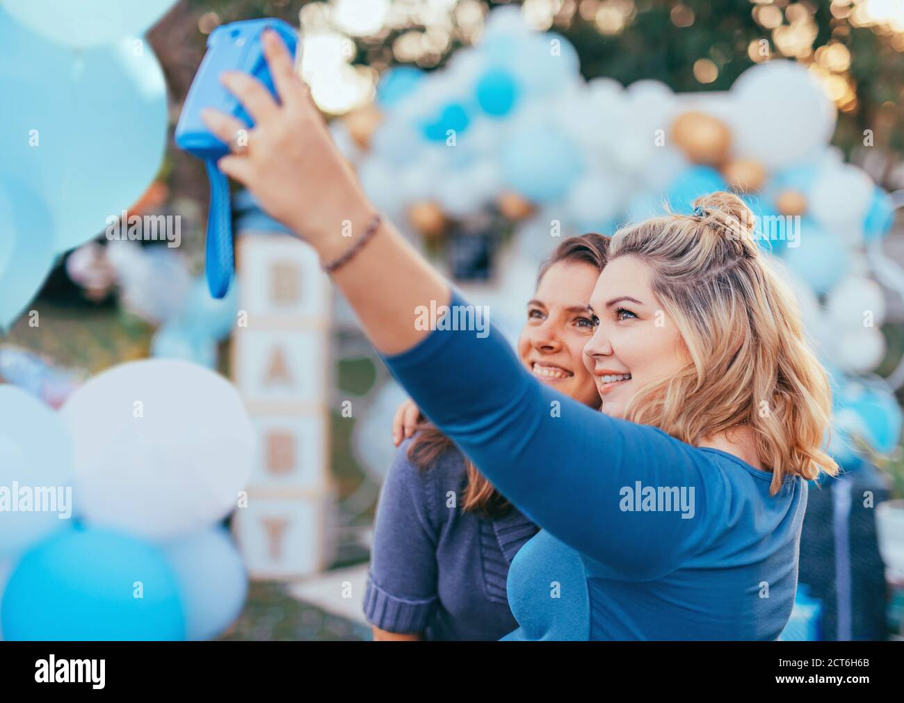 Female friends taking selfie with pregnant woman at a baby shower. Mobile photography, party decorations in white and blue colors, baby boy Stock Photo