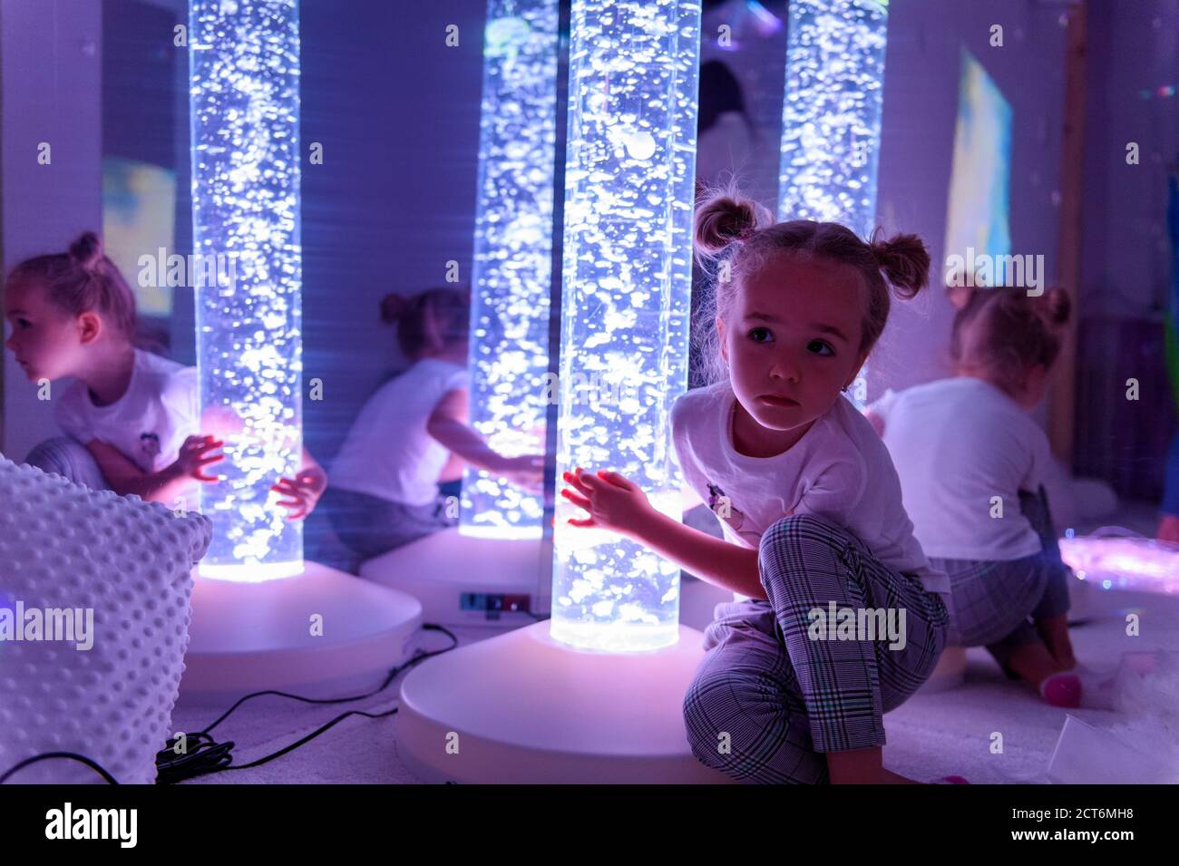 Child in therapy sensory stimulating room, snoezelen. Autistic child interacting with colored lights bubble tube lamp during therapy session. Stock Photo