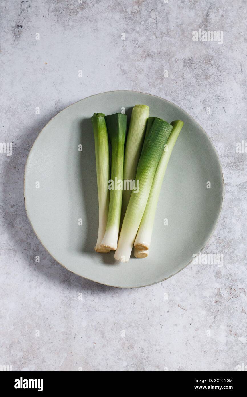 Bunch of baby leeks on a pale blue plate on a grey textured backdrop. Stock Photo