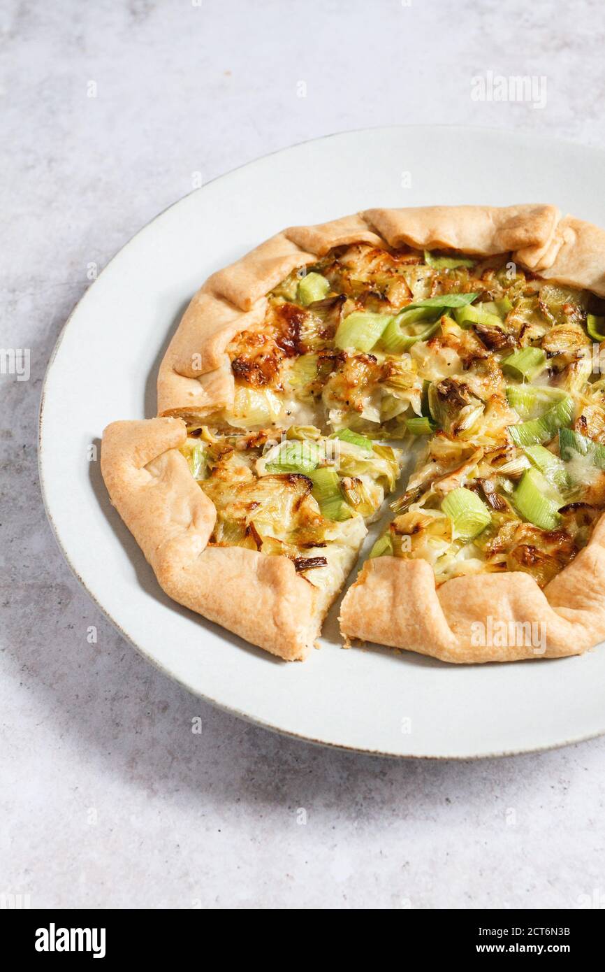Leek and Comté cheese galette. A vegetarian seasonal savoury pastry on a large pale blue plate with a grey textured backdrop. Stock Photo