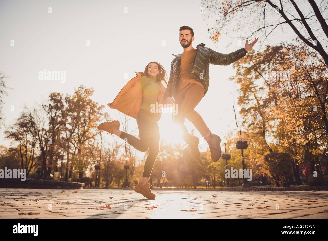 Low angle view full length photo of cheerful two young people girl guy hold hand jump in autumn october town park Stock Photo