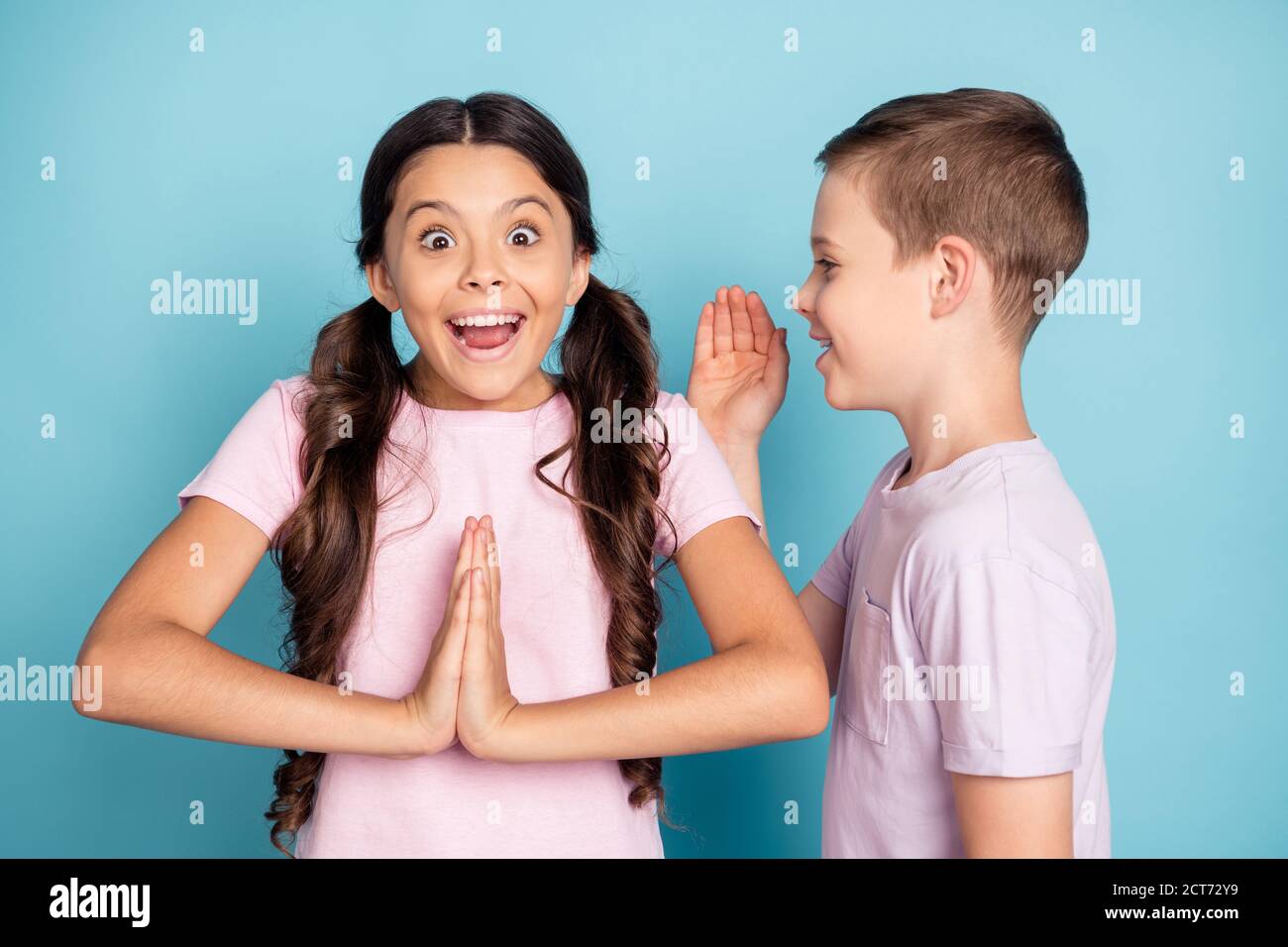 Photo excited two little kids boy whisper hands ear girl secret birthday present impressed put hands together scream cant wait wear casual pink violet Stock Photo