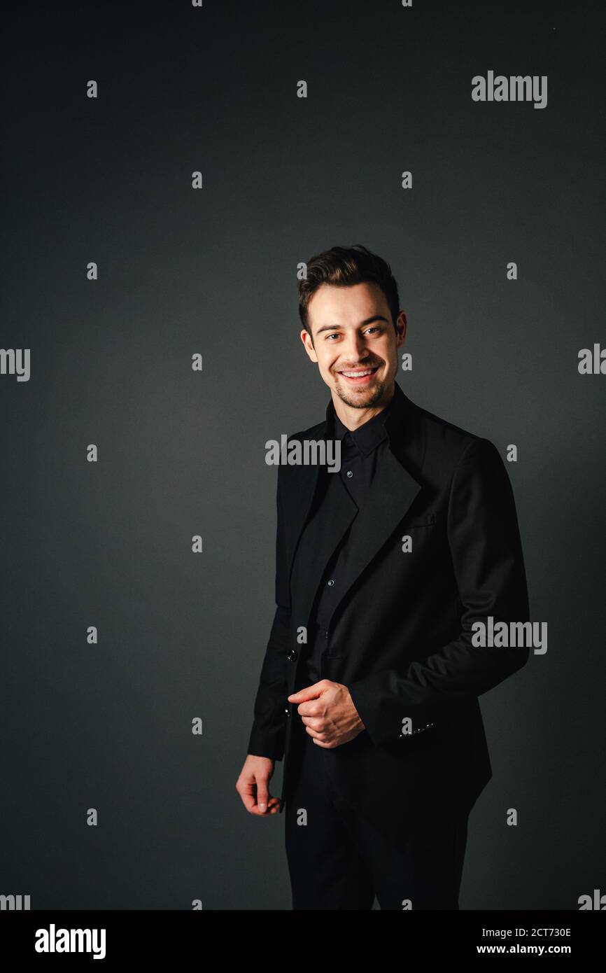 Young handsome man in a black suit, smiling and looking at the camera ...