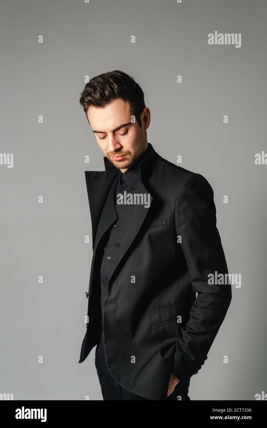 Portrait of a young handsome man in a black suit, standing and looking ...