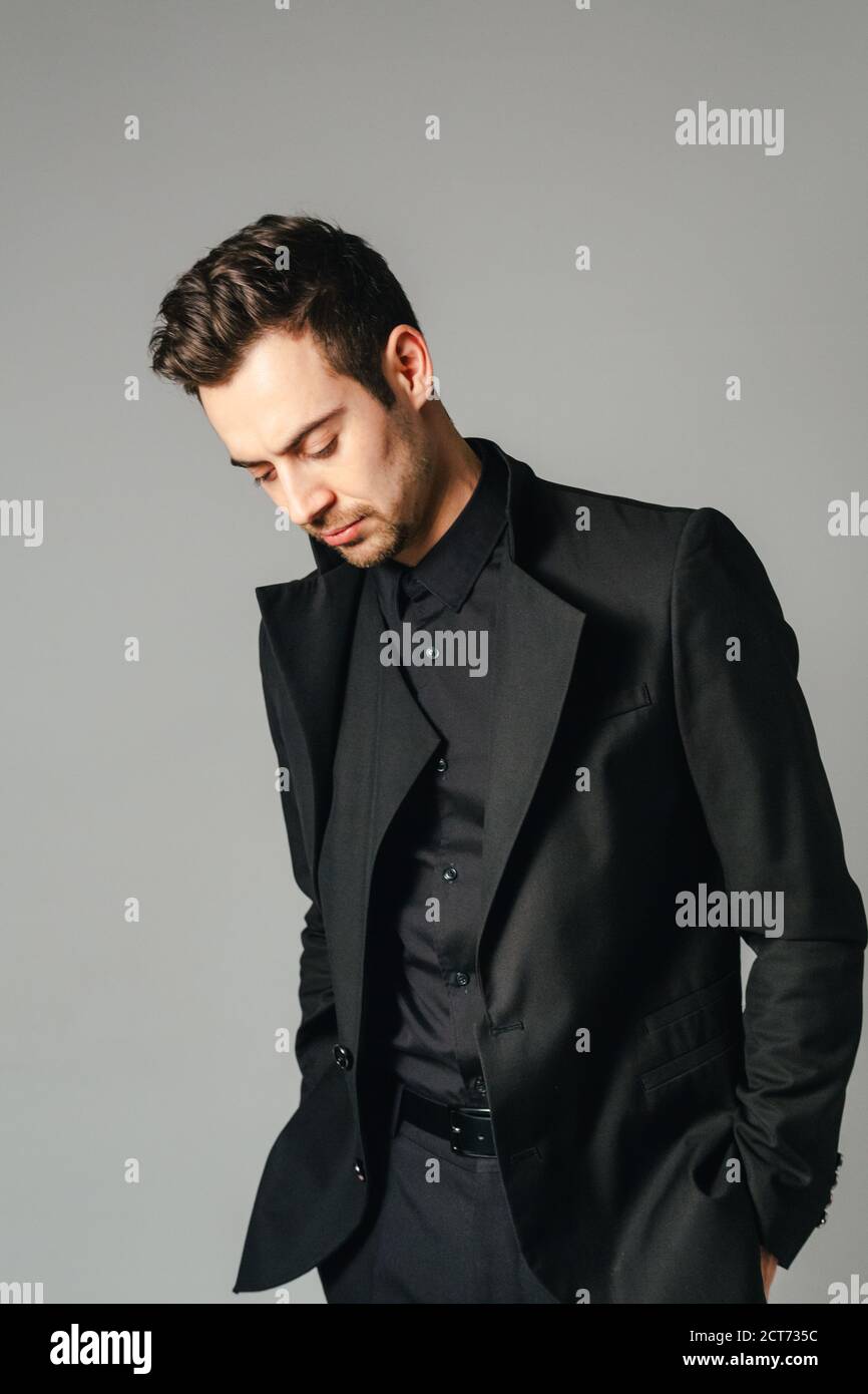 Portrait of a young handsome man in a black suit, standing and looking ...
