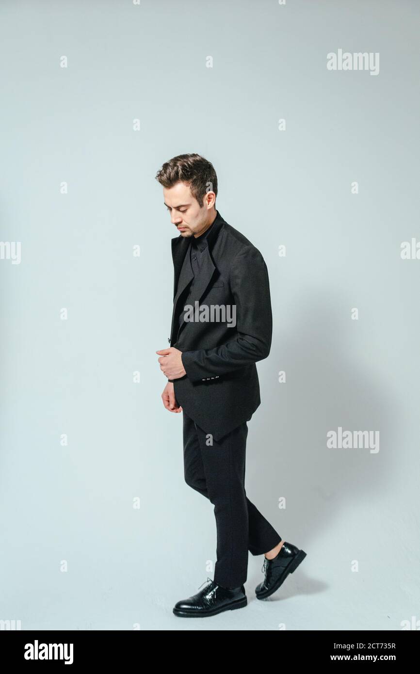 Portrait of a young handsome man in a black suit, standing and looking ...