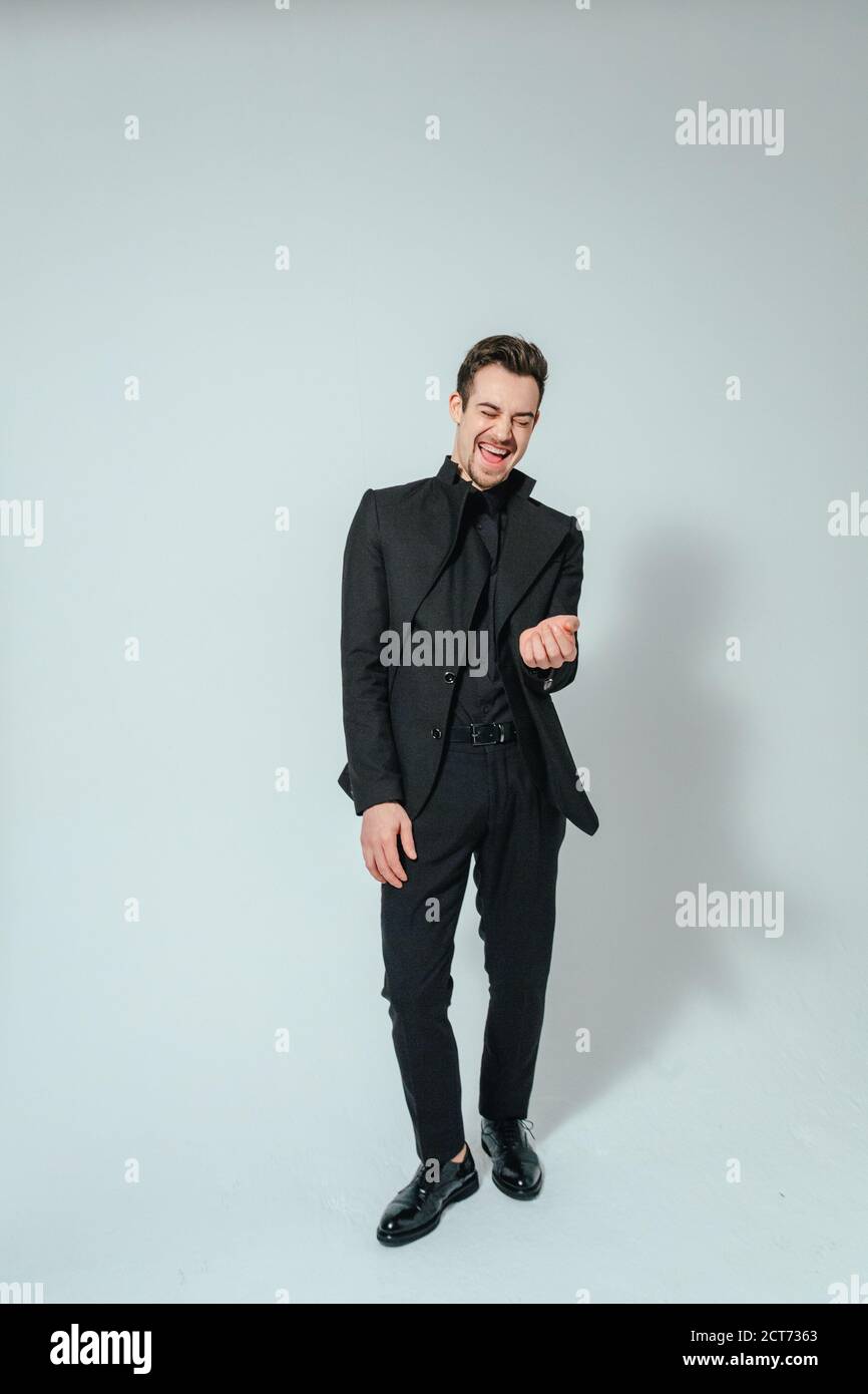 Portrait of a young handsome man in a black suit, laughing, eyes closed ...