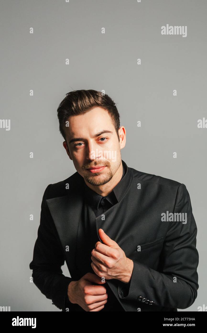 Young handsome man in a black suit, looking at the camera, against plain studio background Stock Photo