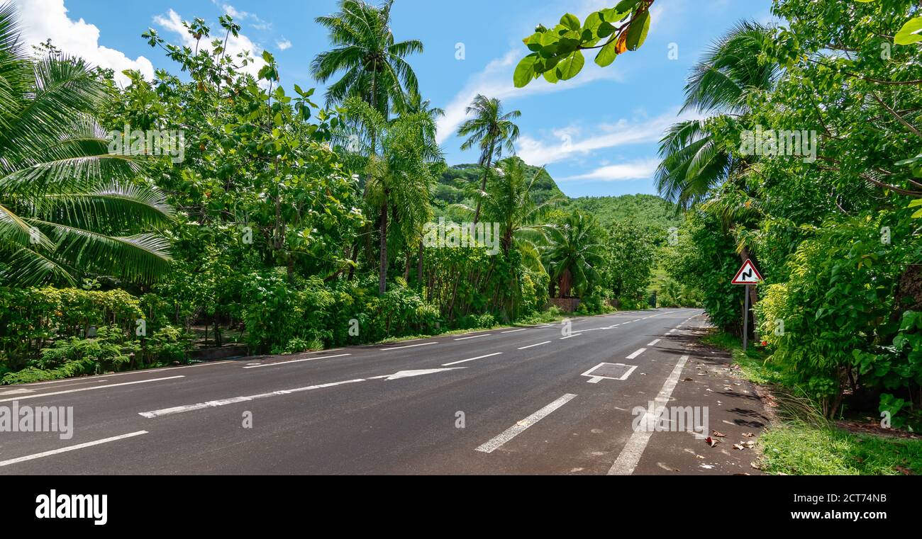 Moorea landscape with an empty asphalt road and a red warning traffic sign with a double bend. Stock Photo