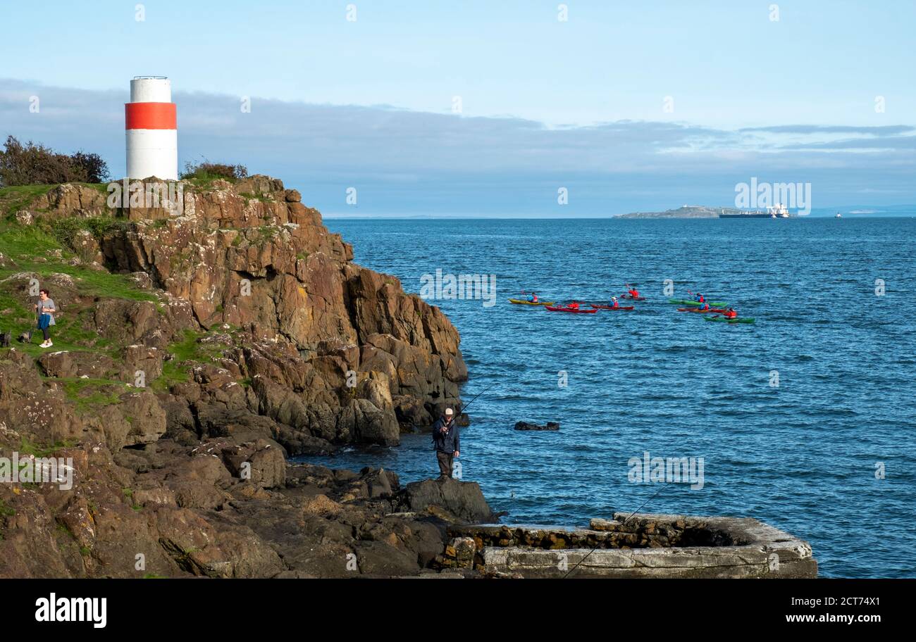 Sea Kayakers pass as people fish from a rocky outcrop on the Fife coastline near Aberdour, Scotland. Stock Photo