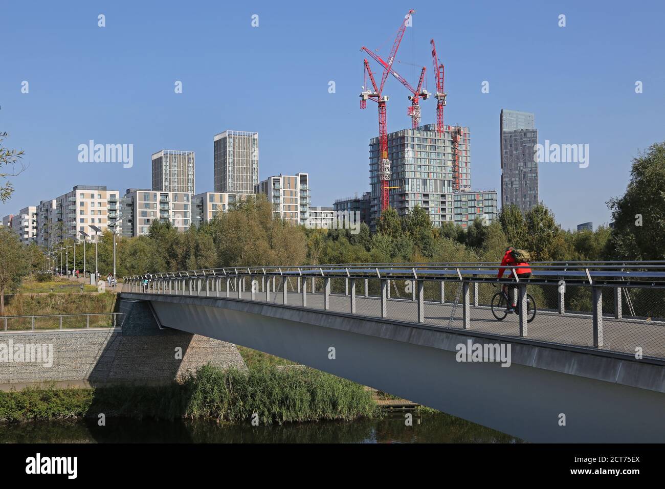 Queen Elizabeth Olympic Park, London. Cyclists on East Cross bridge. Cranes beyond as more apartment blocks are added to the Olympic Village site. Stock Photo