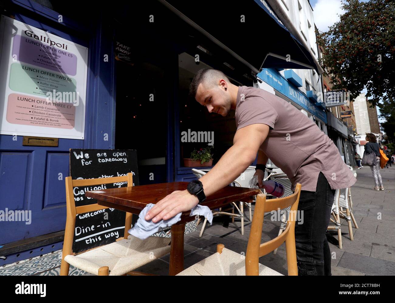 A member of staff cleans the tables outside the Gallipoli restaurant on Upper Street in Islington, North London. Stock Photo