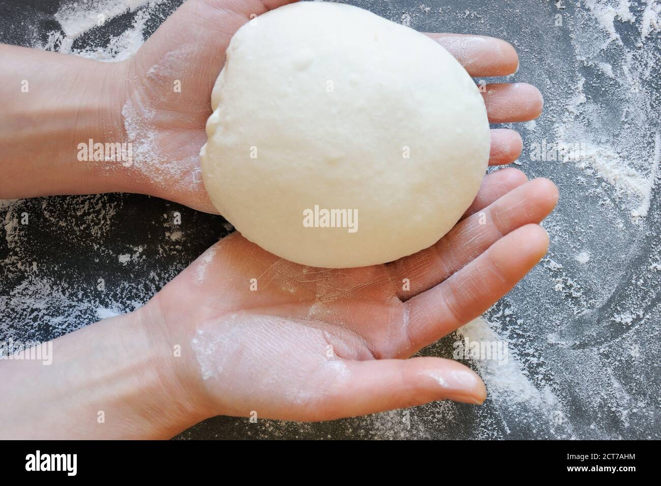 Hands holding a ball of dough over floured background. Dough ready to prepare a delicious homemade meal. Horizontal orientation. Stock Photo