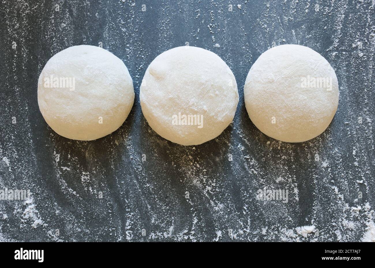 Three balls of fresh homemade wheat dough on kitchen table. Home baking. Dough for pizza cooking, pasta dumplings or bread.Horizontal. Stock Photo