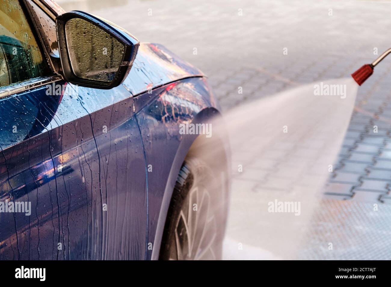 Side view of a blue car washing under high pressure water. Self service
