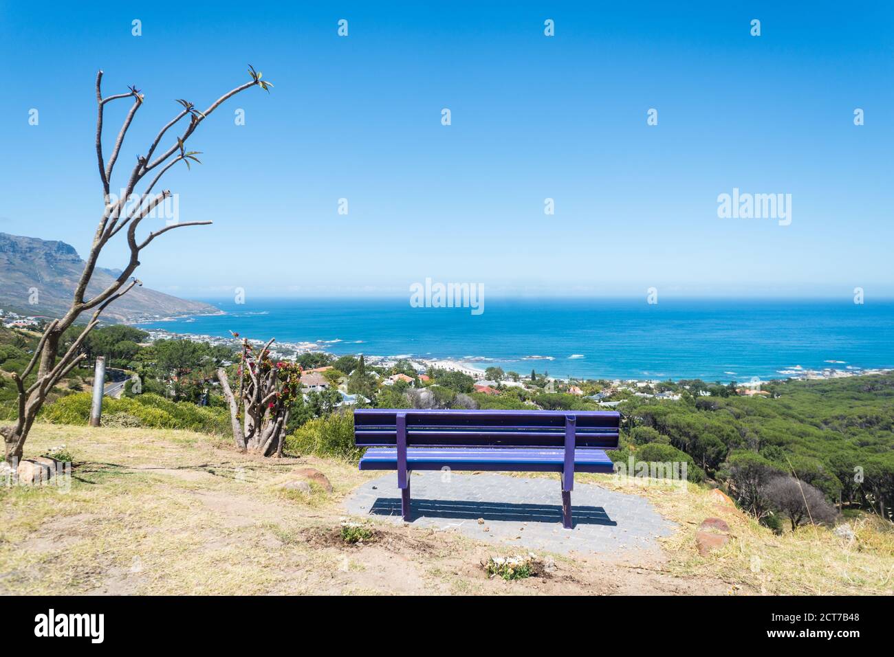 an empty bench on a hill overlooking a spectacular sea view on a Summer day with blue sky and no clouds in Camps Bay, Cape Town, South Africa Stock Photo