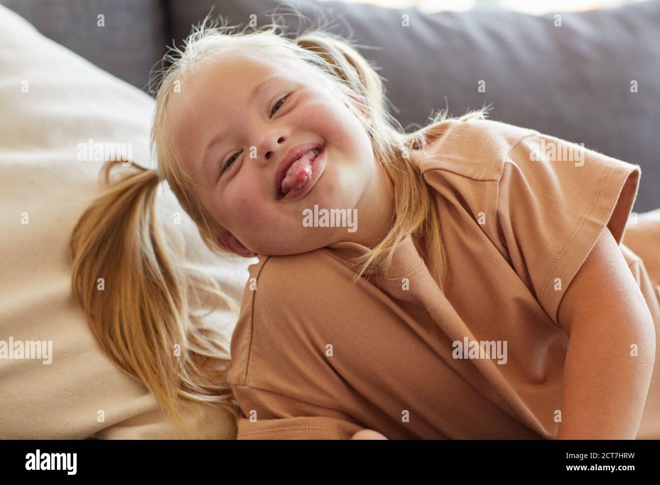 Portrait of carefree little girl with down syndrome sticking tongue out while grimacing for camera Stock Photo