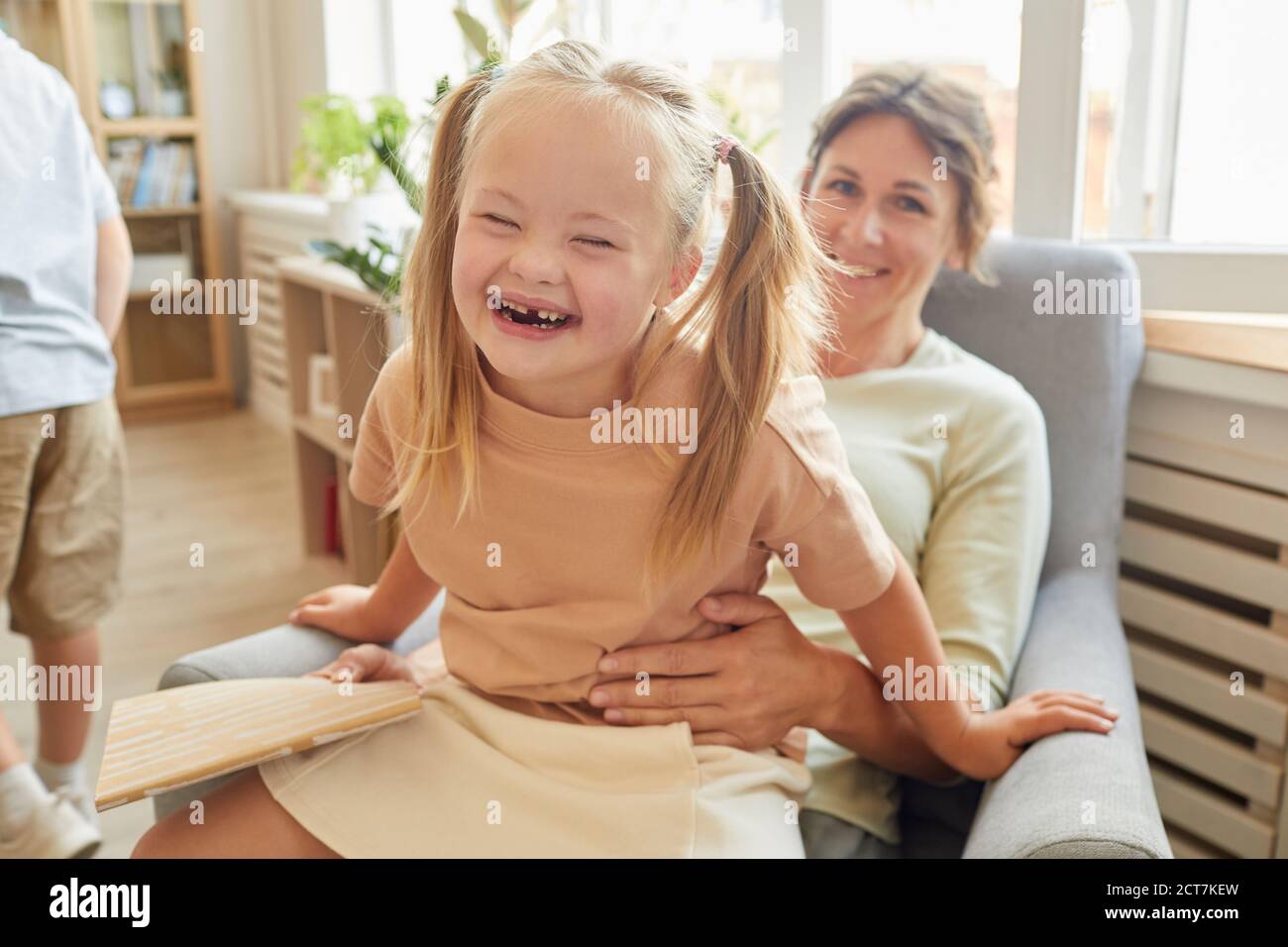 Portrait of cute girl with down syndrome laughing happily while playing with mother at home Stock Photo