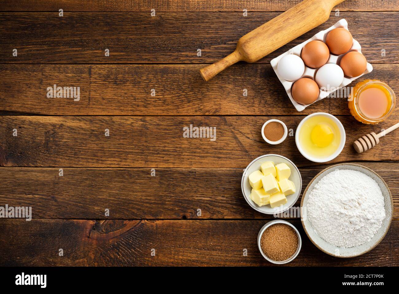 Cooking baking ingredients on a wooden table background. Flour eggs butter sugar and other pastry ingredients on wood. Top view copy space Stock Photo